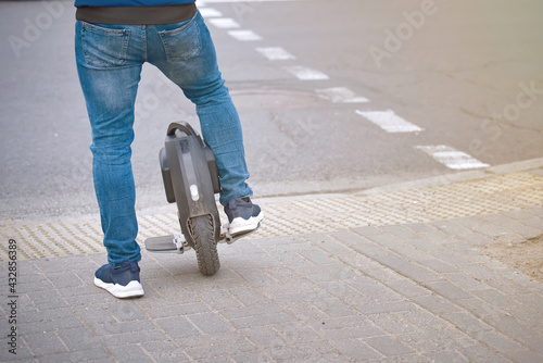 Electric unicycle, man in jeans and sneakers commuting to work on monowheel. Portable individual transportation vehicle. Electric motor transport for daily movement around city. Electric device.