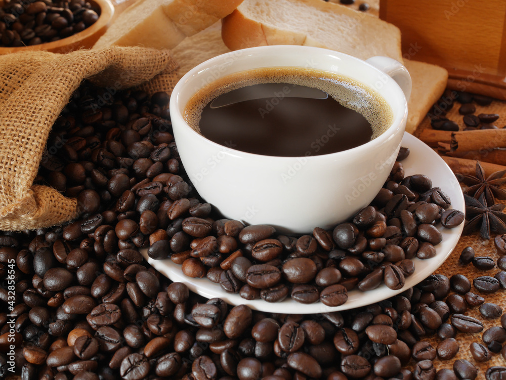 Fototapeta premium A white cup of hot aroma coffee and a sack of coffee beans with some breads for drink and eat in the morning