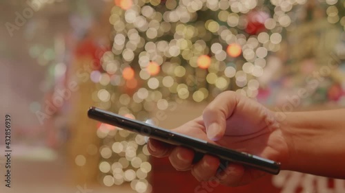 A close-up shot of a woman's hand is holding and using a smartphone with bokeh light are blurred in the background.