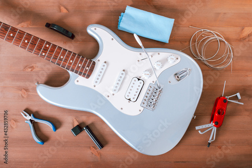 Electric guitar body, new strings and various guitar tools for maintenance and restringing on wooden table top photo