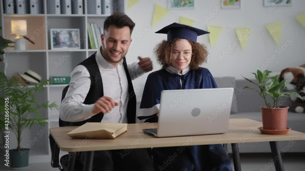 online diploma, happy young woman in academic mantle and hat hugs her boyfriend during graduation ceremony receiving via video link on laptop
