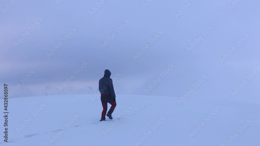 Hiker walks alone on snow in the mountains during winter in a foggy day Hiker walks alone on snow in the mountains during winter in a foggy day