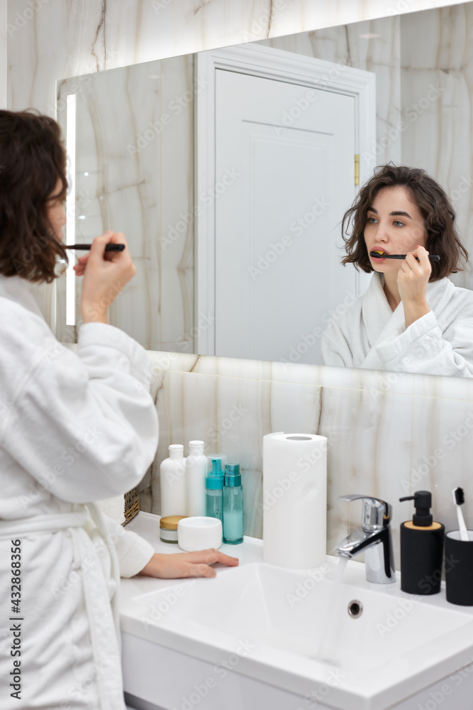 woman in white bathrobes brushing teeth in front of mirror woman in white bathrobes brushing teeth in front of mirror