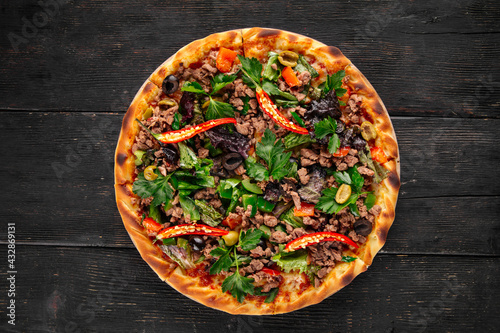 Pizza with spicy peppers and minced meat on the dark wooden background