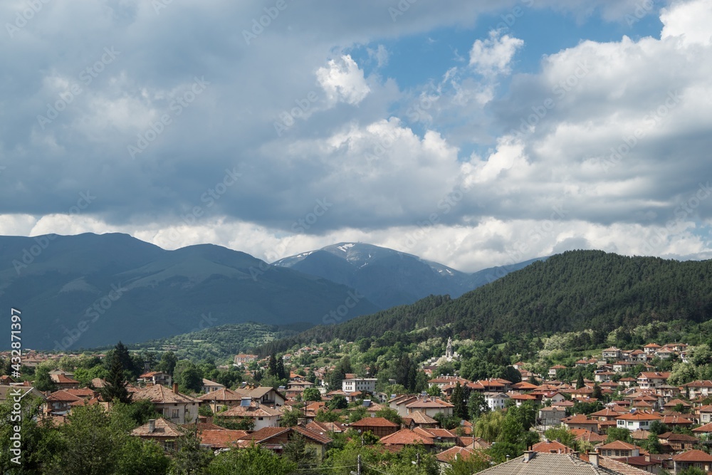 Panoramic natural landscape, town with old typical traditional houses, red roofs, against green mountain hills. High dynamic contrast, dramatic clouds. Bulgaria, Kalofer, Balkan Mountains, Botev peak.