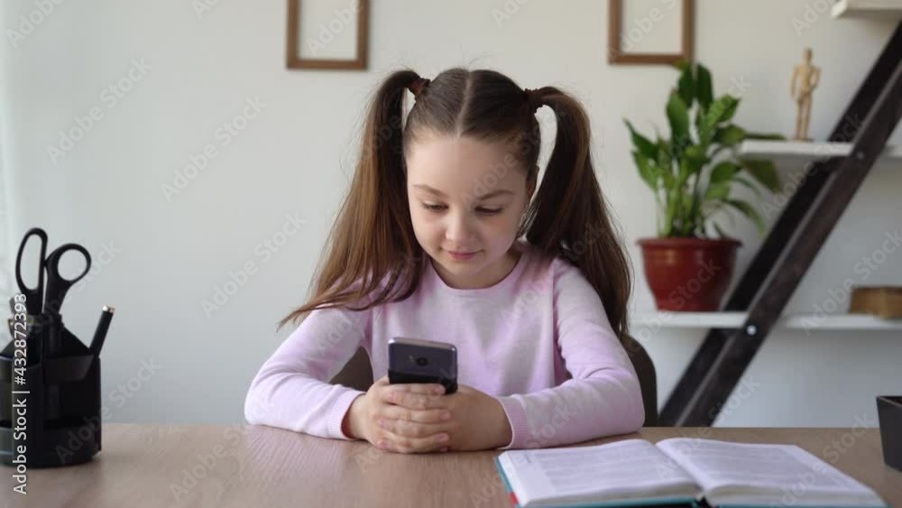 Pupill obsession girl from social networks and the Internet with a phone in her hands sitting at a desk in a room studying online remotely with a gadget. Pupill obsession girl from social networks and the Internet with a phone in her hands sitting at a desk in a room studying online remotely with a gadget.