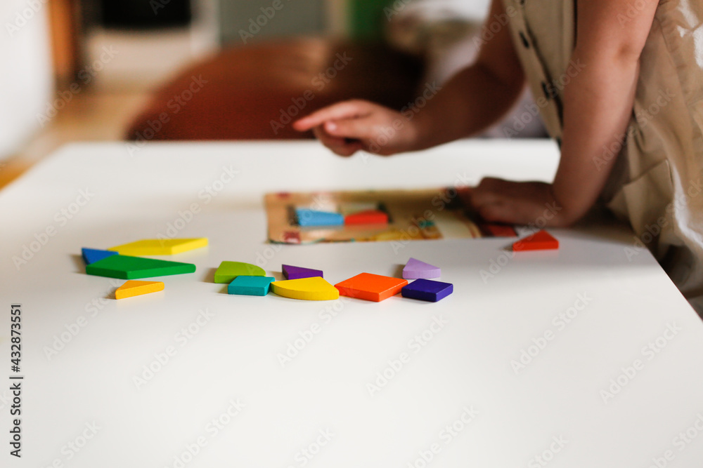 Cute caucasian child toddler playing with a wooden mosaic on the table, earlier child development and children's games, kid playing with a puzzle close-up, toning