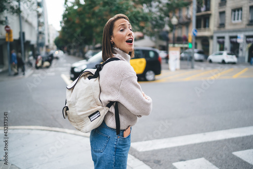 Amazed female tourist with backpack standing at urban setting and feeling shocked during international vacations for getaway, excited Caucasian woman with open mouth looking away and impressing © BullRun