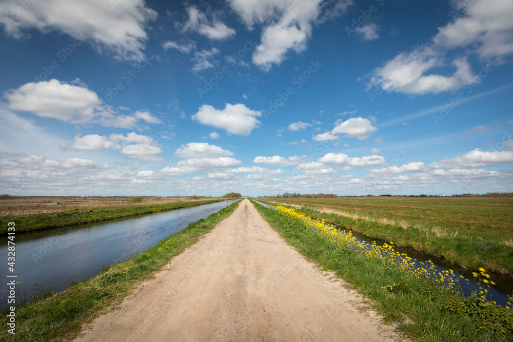 Dutch landscape with a small road / cycling path, along a canal with blue sky and clouds, province Groningen, the Netherlands