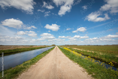 Dutch landscape with a small road / cycling path, along a canal with blue sky and clouds, province Groningen, the Netherlands