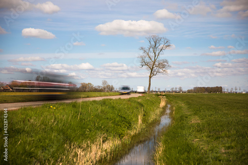 View over a Dutch landscape with a canal, grass, blue sky, white clouds and a small road