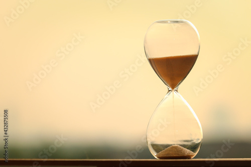 Sand clock measuring time with orange sky in evening time over city blurred background, yellow sand falling down in hourglass old classic timer.