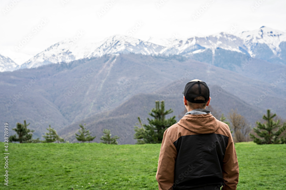 young man in cap from behind looking view of snow capped peak Caucasus mountains, travel, mountain landscape, beauty in nature