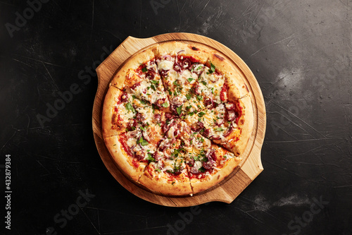 pizza on a wooden base on a black textured background top view