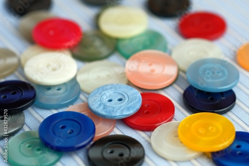 Sewing buttons.Close-up. A decorative element in clothing design. Multi-colored plastic buttons with two holes on a blue-and-white striped cotton fabric.