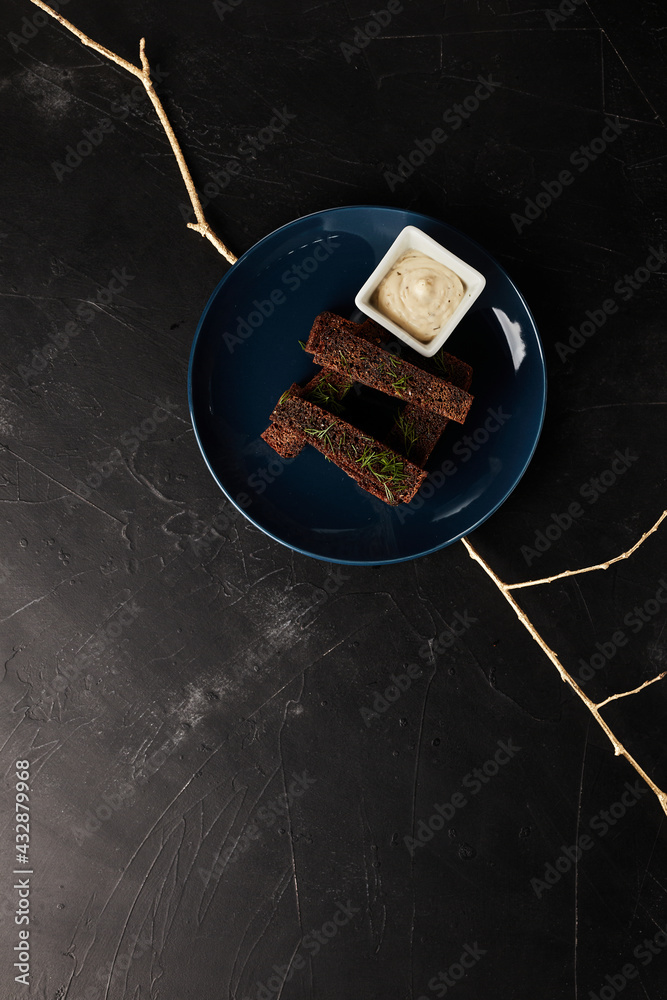 fried rye bread croutons on a blue plate with sauce on a black textured background top view