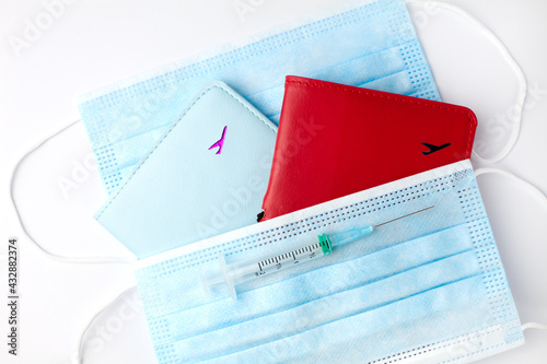 Safe travel concept. Influenza and coronavirus vaccination. Syringe with vaccine, two passports and two protective masks on a white background. Close-up. photo