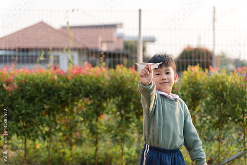 Asian boy playing with a paper airplane at the house yard