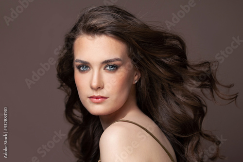 Portrait of beautiful young woman with blowing long healthy dark hair and clear skin on brown background