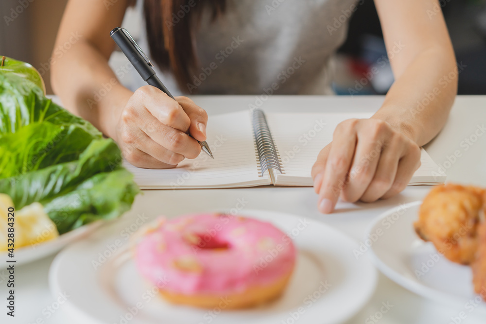 Diet, Dieting young asian woman work, write diet plan for right nutrition, eat vegetables, salad is food for good health more than choose donut, junk food. Nutritionist female, Weight loss person..