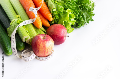 Cucumbers, celery, carrots, green lettuse, red apples and measure tape isolated on a white background. Fruit and vegetables. Diet, wellness and weight loss concept. Healthy lifestyle. Good nutrition photo