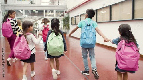 Medium shot of children walking in school hallway. Schoolkids looking around. Boy in eyeglasses pulling little girl by hand. Shooting from behind. Education, back to school concept.