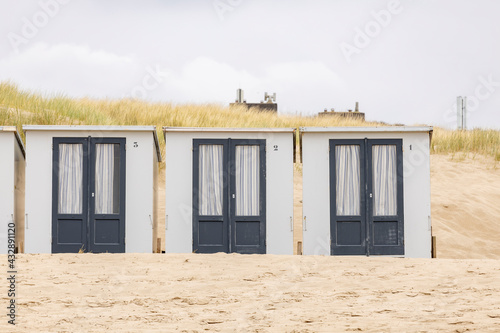 Picturesque coastal scenery with row of small closed square summer cubicle homes on Dutch North sea beach with dune behind on an overcast day photo