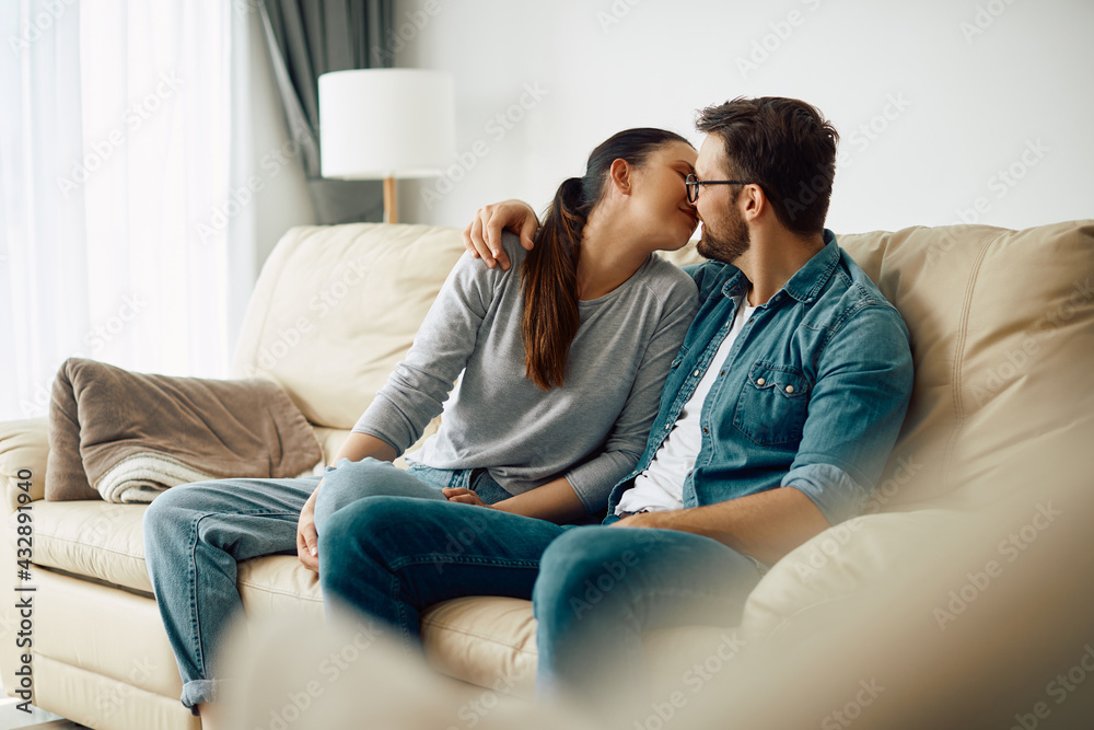 Affectionate couple kissing while relaxing on the sofa at home.