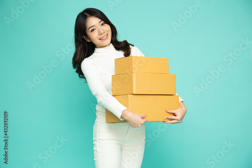 Happy Asian woman smiling and holding package parcel box isolated on green background, Delivery courier and shipping service concept © comzeal