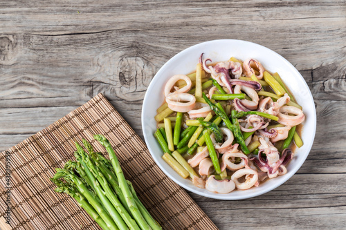 Stir Asparagus with Squid on table in restaurant. Stir-fried asparagus in white plate on wooden table. Thai food , Asparagus stir fried with Squid.