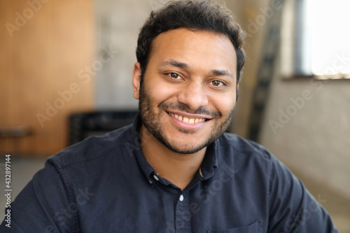 Cheerful and serene hindu man in smart casual shirt, headshot of young handsome indian guy, handsome mixed-race male looks at the camera with toothy smile