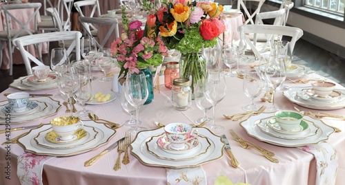 Table set up for bridal shower on bright spring day with flowers in the middle and vintage tea cups on each plate