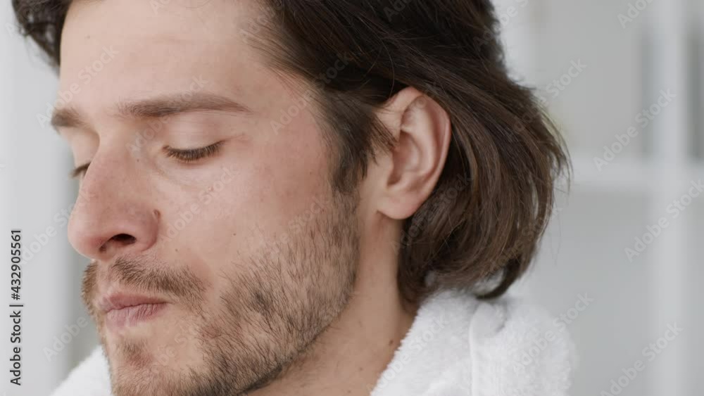 Close up portrait of young exhausted guy wiping sweat from face and drinking water after training at home, slow motion