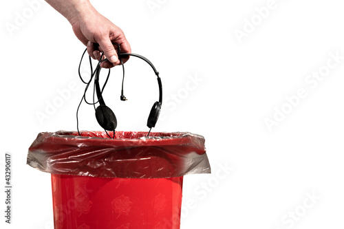 A man throws old wired headphones into the trash can. Male hand throws unnecessary headphones into the trash on a white background close-up.