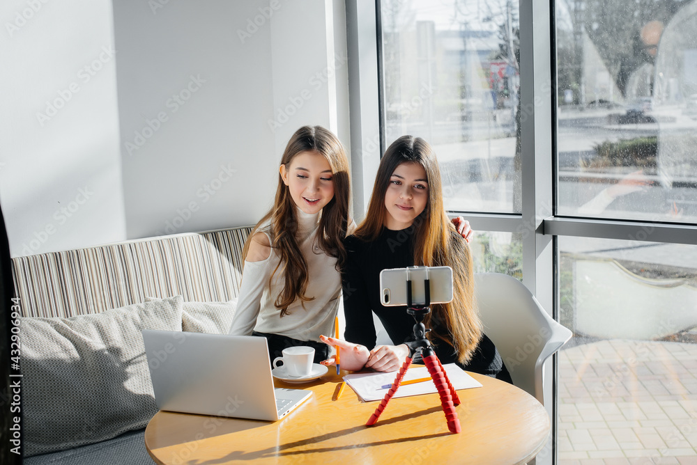 Two young beautiful girls are sitting in a cafe, recording video blogs and communicating on social networks. Two young beautiful girls are sitting in a cafe, recording video blogs and communicating on social networks.