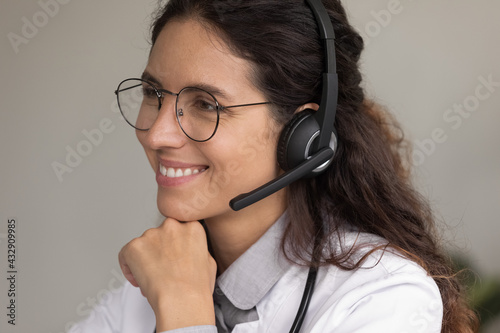 Doc speaking. Friendly young hispanic woman medical consultant gp wear glasses modern wireless headphones take patients calls. Smiling female doctor healthcare helpline worker ready to assist online