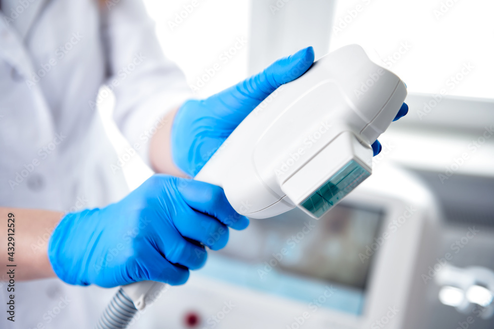 Beautician's hands in blue gloves holding a medical laser head for rejuvenating face and body treatments Beautician's hands in blue gloves holding a medical laser head for rejuvenating face and body treatments
