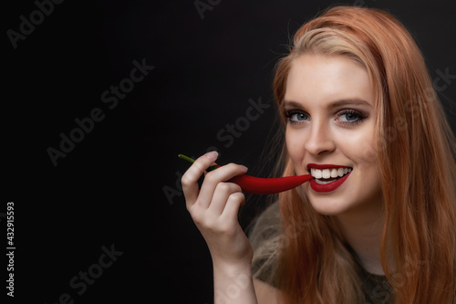 Low key portrait of smiling attractive  long hair young woman tasting chili pepper. 