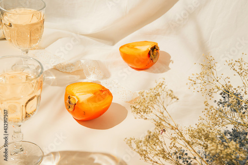 Stampa su tela Halfs of persimmon fruits and two glasses with lemonade on pastel background with white cloth and sunlit