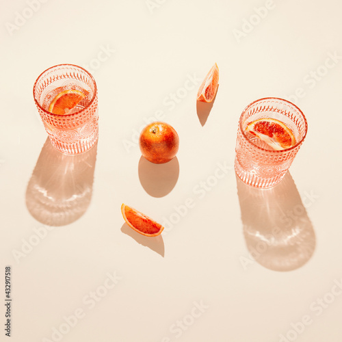 Bloody oranges and glasses of fresh lemonade or water on on pastel beige backgound. Summer refreshment concept. Sunlit flat lay. Minimal style. Top view