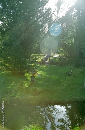 Summer garden with sunlight flares. Urns and small bridge over stream. Garden seat. Lake in foreground
