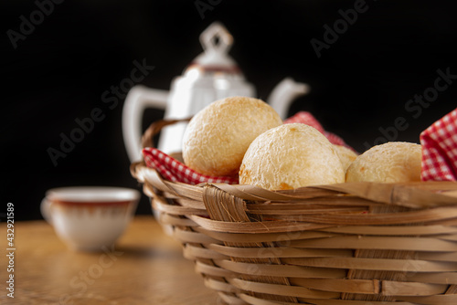 Brazilian cheese bread, checkered cloth basket with cheese breads on rustic wood with teapot and cup of coffee in the background, selective focus. © Milton Buzon