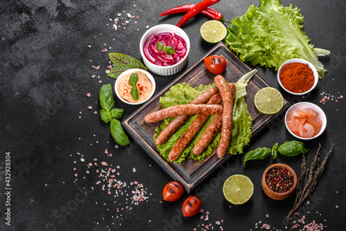 Tasty grilled sausages with spices and herbs on a wooden board on a dark concrete background