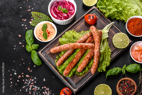 Tasty grilled sausages with spices and herbs on a wooden board on a dark concrete background