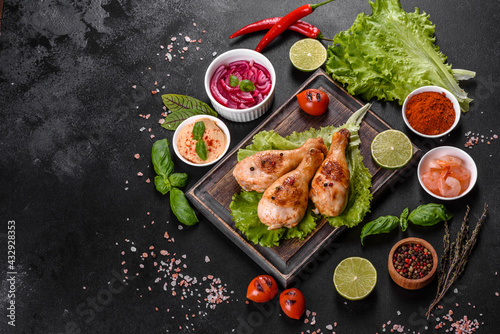 Tasty grilled chicken legs with spices and herbs on a wooden board on a dark concrete background