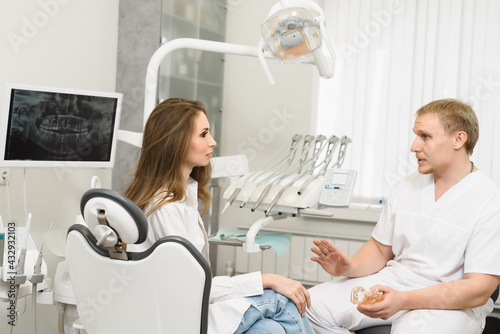 Male dentist doctor talking with woman patient and showing a dental model in modern dentistry