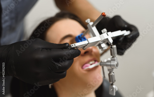 An experienced dentist placing a facial bow for woman patient to examine the bite. Modern technologies in dental treatment