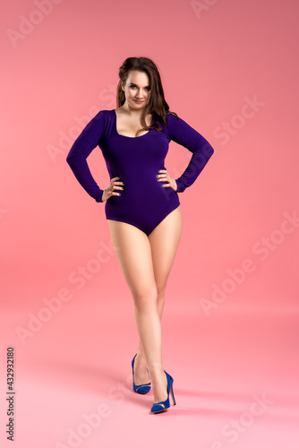 Sexy plus size model with big breasts in purple bodysuit on pink background