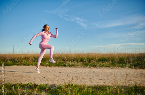 Young sporty woman in pink sportswear running outdoors on a beautiful sunny early summer day