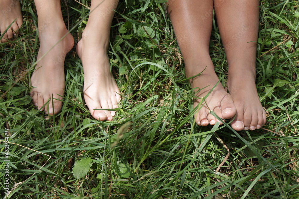 Alternative school lesson outside in nature, a group of children sitting barefoot in the green grass at a sunny day, kids friendship forever